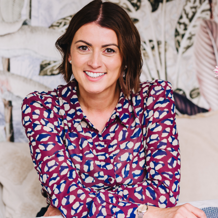 A picture of Aimee Bateman, a middle-aged white woman with short brown hair. Aimee is wearing a floral print shirt. She is smiling.